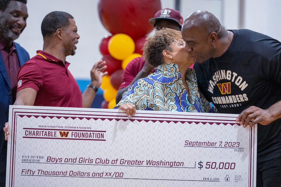 Washington Commanders part-owner Magic Johnson, right, gets a kiss from Gabrielle Webster, CEO...